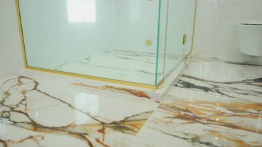 Cilalanmış mermer banyo zemininde altın kaplamalı modern cam bir duş. Lüks iç tasarım, temiz mimari ve zarif banyo tadilatı. Yüksek kalite 4k görüntü