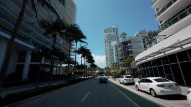 POV 'un hızlandırılmış sürüşü, altında yüksek binalar ve palmiye ağaçları bulunan modern bir kıyı şehrinde rahat şehir hareketlerini ve tropikal manzarayı gösteriyor. USA IL Miami 01 Nisan 2025. Yüksek kalite 4k görüntü