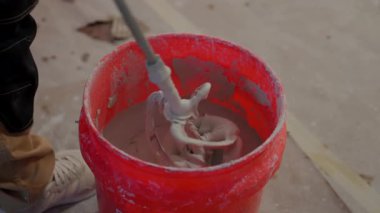 Elektrik mikseri kullanarak havan topunu kırmızı kovaya karıştıran bir işçi POV 'u. Tadilat, inşaat hazırlığı ve kullanımda olan profesyonel inşaat araçlarını kapatın. Yüksek kalite 4k görüntü