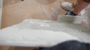 Profesyonel işçinin tenceresi seramik fayansa kalın bir katman yapıştırarak duvara yapıştırıyor. Yenileme işleri, inşaat hazırlıkları ve inşaat aletleri. Yüksek kalite 4k görüntü