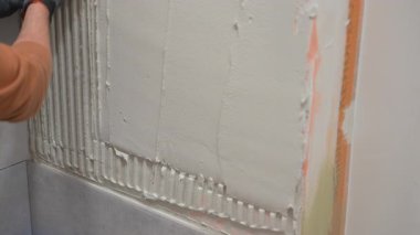 Profesyonel inşaat işçisi, seramik fayansı yapıştırmak için kalın yapıştırıcı tabakasını duvara yapıştırıyor. Yenileme işleri, inşaat hazırlıkları ve inşaat aletleri. Yüksek kalite 4k görüntü
