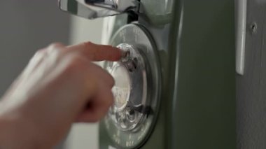 Eski bir döner telefondan numara çeviren bir parmağın yakın çekimi. Sahne klasik iletişim, retro teknoloji ve eski moda telefon kullanımını temsil ediyor. Yüksek kalite 4k görüntü