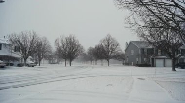 Huzurlu bir banliyö sokağına hafif kar yağar evler, park edilmiş arabalar, çıplak kış ağaçları. Soğuk hava, kış atmosferi ve sakin yaşam. Yüksek kalite 4k görüntü