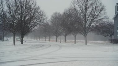 Huzurlu bir banliyö sokağına sert kar yağar, evi ve çıplak kış ağaçları vardır. Soğuk hava, kış atmosferi ve sakin yaşam. Yüksek kalite 4k görüntü