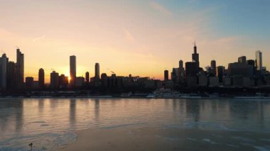 Kışın Michigan Gölü 'yle Chicago silueti. İnce buz örtüleri ve yüzen donmuş oluşumlar su yüzeyini kaplarken sıcak altın ışık şehrin gökdelenlerinden yansıyor. Yüksek kalite 4k görüntü