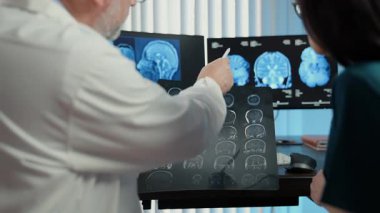 Doktorlar beyin MR taramalarını inceliyor ve modern klinikte birden fazla monitör duruyor, gelişmiş nörogörüntüleme teknolojisi ve sağlık tanısı konsepti. Yüksek kalite 4k görüntü