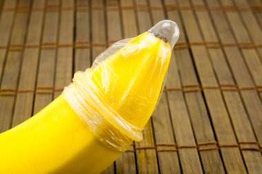 Banana with condom on wooden background clipart