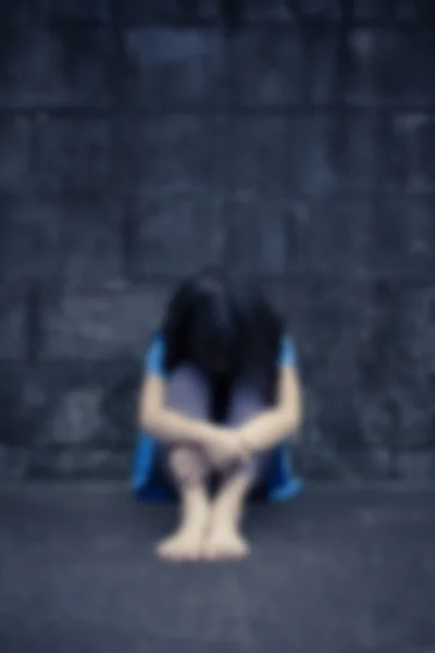 Liten flicka förtvivlan sitter mot en tegelvägg, rörelse blurr — Stockfoto