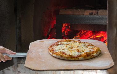  Hand pushing the finished pizza from the oven with the pizza sh