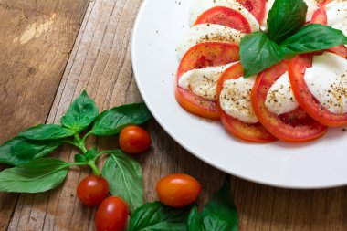 Mozzarella soslu Caprese salatası, domates, beyaz tabakta fesleğen.