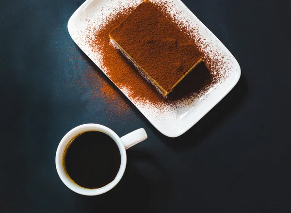 Bolo tiramisu saboroso com xícara de café no fundo preto — Fotografia de Stock