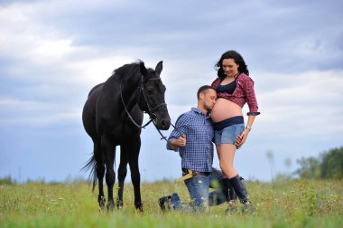 Mutlu çift - uzun saçlı, uzun saçlı, yakışıklı esmer; adam dizlerinin üzerinde, onun göbeğini öpüyor ve siyah atın dizginlerini tutuyor. Meadow, arkasında harika bir gökyüzü