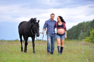 Çocuğunu bekliyor. Genç bir çift - uzun saçlı esmer, hamile; uzun boylu ve cesur, siyah atın dizginlerini tutan, çiftlikte bir yürüyüş.