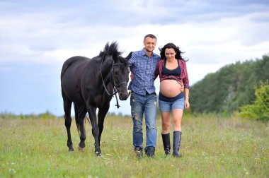 Çocuğunu bekliyor. Genç bir çift - uzun saçlı esmer, hamile; uzun boylu ve cesur, siyah atın dizginlerini tutan, çiftlikte bir yürüyüş.