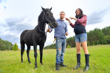 Çocuğunu bekliyor. Genç çift - uzun saçlı, esmer, yakışıklı ve hamile; uzun boylu ve cesur, siyah atın dizginlerini tutan, mavi gökyüzüne karşı çayırda bir yürüyüş