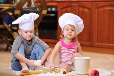 İki kardeş - erkek ve kız - şöminenin yanında aşçı şapkası takmış mutfakta un ile kirlenmiş, yemekle oynuyor, ortalığı dağıtıyor ve eğleniyorlar.