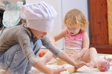 İki kardeş - erkek ve kız - şöminenin yanında aşçı şapkası takmış mutfakta un ile kirlenmiş, yemekle oynuyor, ortalığı dağıtıyor ve eğleniyorlar.