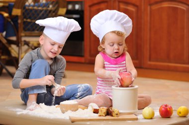 İki kardeş - erkek ve kız - şöminenin yanında aşçı şapkası takmış mutfakta un ile kirlenmiş, yemekle oynuyor, ortalığı dağıtıyor ve eğleniyorlar.