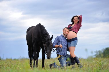 Mutlu çift - uzun saçlı, uzun saçlı, yakışıklı esmer; adam dizlerinin üzerinde, onun göbeğini öpüyor ve siyah atın dizginlerini tutuyor. Meadow, arkasında harika bir gökyüzü