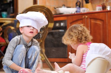 İki kardeş - erkek ve kız - şöminenin yanında aşçı şapkası takmış mutfakta un ile kirlenmiş, yemekle oynuyor, ortalığı dağıtıyor ve eğleniyorlar.