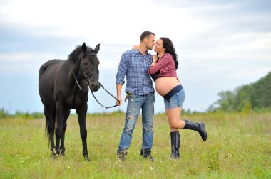 Çocuğunu bekliyor. Genç bir çift - uzun saçlı esmer, hamile; uzun boylu ve cesur, siyah atın dizginlerini tutan, çiftlikte bir yürüyüş.