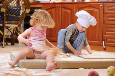 İki kardeş - erkek ve kız - şöminenin yanında aşçı şapkası takmış mutfakta un ile kirlenmiş, yemekle oynuyor, ortalığı dağıtıyor ve eğleniyorlar.