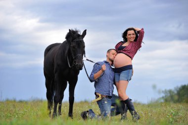 Mutlu çift - uzun saçlı, uzun saçlı, yakışıklı esmer; adam dizlerinin üzerinde, onun göbeğini öpüyor ve siyah atın dizginlerini tutuyor. Meadow, arkasında harika bir gökyüzü