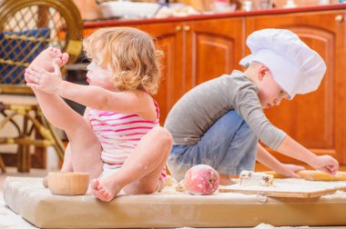 İki kardeş - erkek ve kız - şöminenin yanında aşçı şapkası takmış mutfakta un ile kirlenmiş, yemekle oynuyor, ortalığı dağıtıyor ve eğleniyorlar.