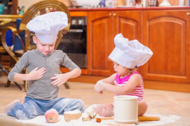 İki kardeş - erkek ve kız - şöminenin yanında aşçı şapkası takmış mutfakta un ile kirlenmiş, yemekle oynuyor, ortalığı dağıtıyor ve eğleniyorlar.