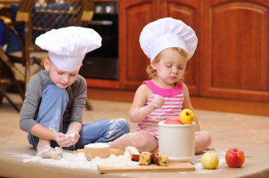 İki kardeş - erkek ve kız - şöminenin yanında aşçı şapkası takmış mutfakta un ile kirlenmiş, yemekle oynuyor, ortalığı dağıtıyor ve eğleniyorlar.