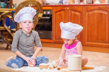 İki kardeş - erkek ve kız - şöminenin yanında aşçı şapkası takmış mutfakta un ile kirlenmiş, yemekle oynuyor, ortalığı dağıtıyor ve eğleniyorlar.