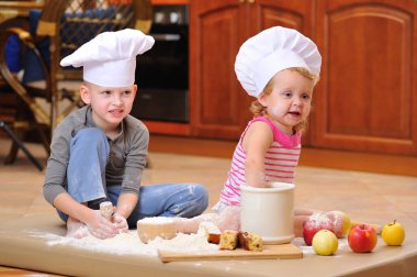 İki kardeş - erkek ve kız - şöminenin yanında aşçı şapkası takmış mutfakta un ile kirlenmiş, yemekle oynuyor, ortalığı dağıtıyor ve eğleniyorlar.