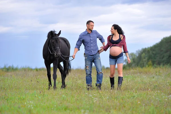 Çocuğunu bekliyor. Genç bir çift - uzun saçlı esmer, hamile; uzun boylu ve cesur, siyah atın dizginlerini tutan, çiftlikte bir yürüyüş.
