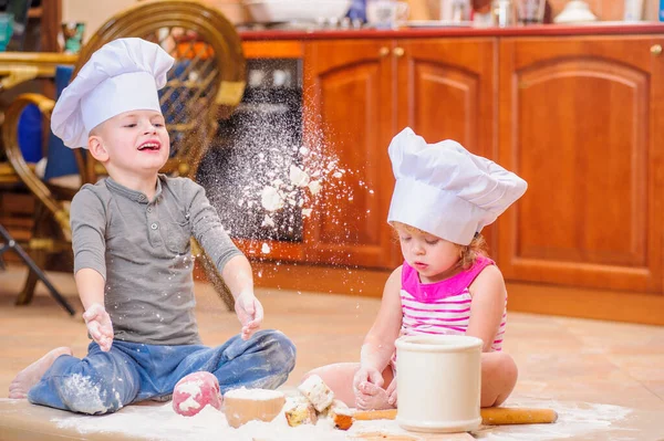 İki kardeş - erkek ve kız - şöminenin yanında aşçı şapkası takmış mutfakta un ile kirlenmiş, yemekle oynuyor, ortalığı dağıtıyor ve eğleniyorlar.