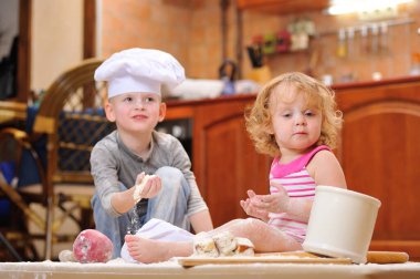 İki kardeş - erkek ve kız - şöminenin yanında aşçı şapkası takmış mutfakta un ile kirlenmiş, yemekle oynuyor, ortalığı dağıtıyor ve eğleniyorlar.