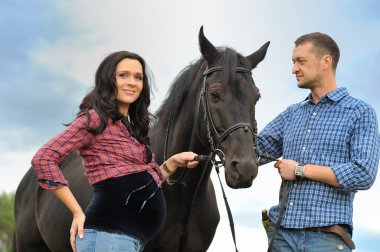 Çocuğunu bekliyor. Genç bir çift - uzun saçlı esmer, hamile; uzun boylu ve cesur, siyah atın dizginlerini tutan, çiftlikte bir yürüyüş.