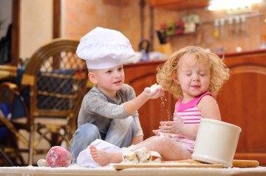 İki kardeş - erkek ve kız - şöminenin yanında aşçı şapkası takmış mutfakta un ile kirlenmiş, yemekle oynuyor, ortalığı dağıtıyor ve eğleniyorlar.