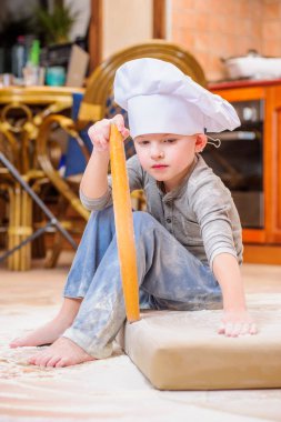 Çocuk mutfakta oturmuş un kirletiyor, yemekle oynuyor, ortalığı dağıtıyor ve eğleniyor.