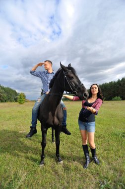 Çocuğu bekliyor, çayırda yürüyor. Ekose fanila gömlekli genç bir çift - uzun saçlı, uzun boylu, yakışıklı bir esmer, adam uzun boylu ve cesur, siyah bir ata biniyor..