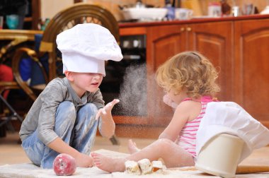 İki kardeş - erkek ve kız - şöminenin yanında aşçı şapkası takmış mutfakta un ile kirlenmiş, yemekle oynuyor, ortalığı dağıtıyor ve eğleniyorlar.