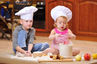 İki kardeş - erkek ve kız - şöminenin yanında aşçı şapkası takmış mutfakta un ile kirlenmiş, yemekle oynuyor, ortalığı dağıtıyor ve eğleniyorlar.