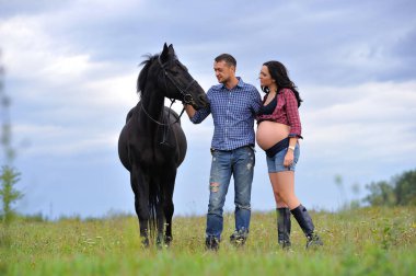 Çocuğunu bekliyor. Genç bir çift - uzun saçlı esmer, hamile; uzun boylu ve cesur, siyah atın dizginlerini tutan, çiftlikte bir yürüyüş.