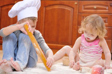 İki kardeş - erkek ve kız - şöminenin yanında aşçı şapkası takmış mutfakta un ile kirlenmiş, yemekle oynuyor, ortalığı dağıtıyor ve eğleniyorlar.