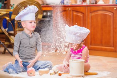 İki kardeş - erkek ve kız - şöminenin yanında aşçı şapkası takmış mutfakta un ile kirlenmiş, yemekle oynuyor, ortalığı dağıtıyor ve eğleniyorlar.