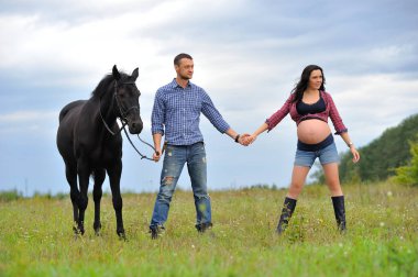 Çocuğunu bekliyor. Genç bir çift - uzun saçlı esmer, hamile; uzun boylu ve cesur, siyah atın dizginlerini tutan, çiftlikte bir yürüyüş.