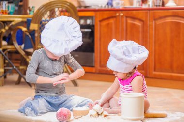 İki kardeş - erkek ve kız - şöminenin yanında aşçı şapkası takmış mutfakta un ile kirlenmiş, yemekle oynuyor, ortalığı dağıtıyor ve eğleniyorlar.