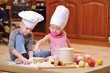 İki kardeş - erkek ve kız - şöminenin yanında aşçı şapkası takmış mutfakta un ile kirlenmiş, yemekle oynuyor, ortalığı dağıtıyor ve eğleniyorlar.