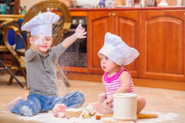 İki kardeş - erkek ve kız - şöminenin yanında aşçı şapkası takmış mutfakta un ile kirlenmiş, yemekle oynuyor, ortalığı dağıtıyor ve eğleniyorlar.