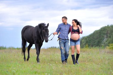 Çocuğunu bekliyor. Genç bir çift - uzun saçlı esmer, hamile; uzun boylu ve cesur, siyah atın dizginlerini tutan, çiftlikte bir yürüyüş.