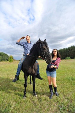 Çocuğu bekliyor, çayırda yürüyor. Ekose fanila gömlekli genç bir çift - uzun saçlı, uzun boylu, yakışıklı bir esmer, adam uzun boylu ve cesur, siyah bir ata biniyor..